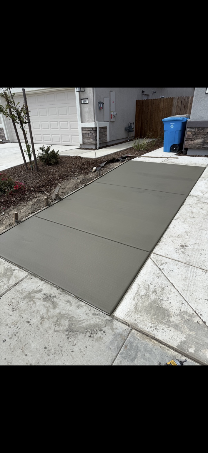 Freshly poured concrete driveway extension alongside a home